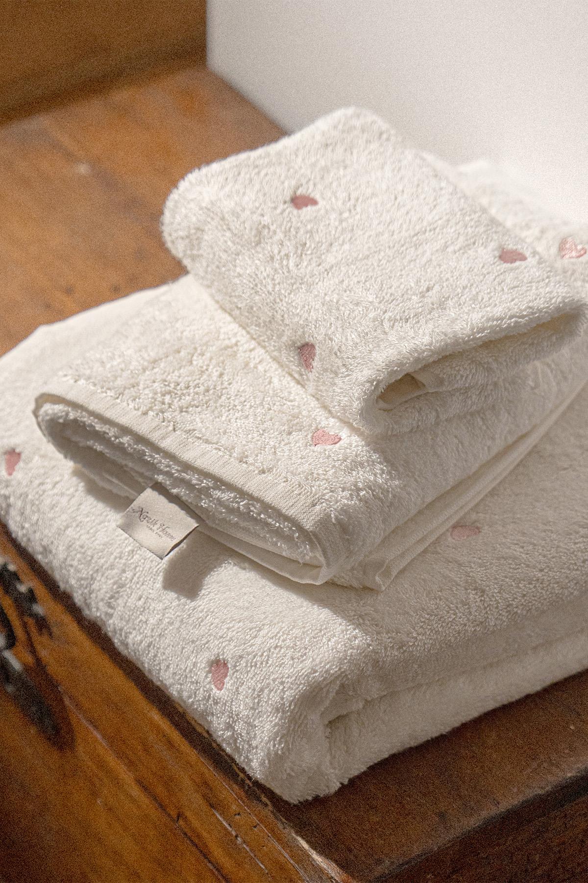 White soft towel set with pink hearts, folded on a wooden surface