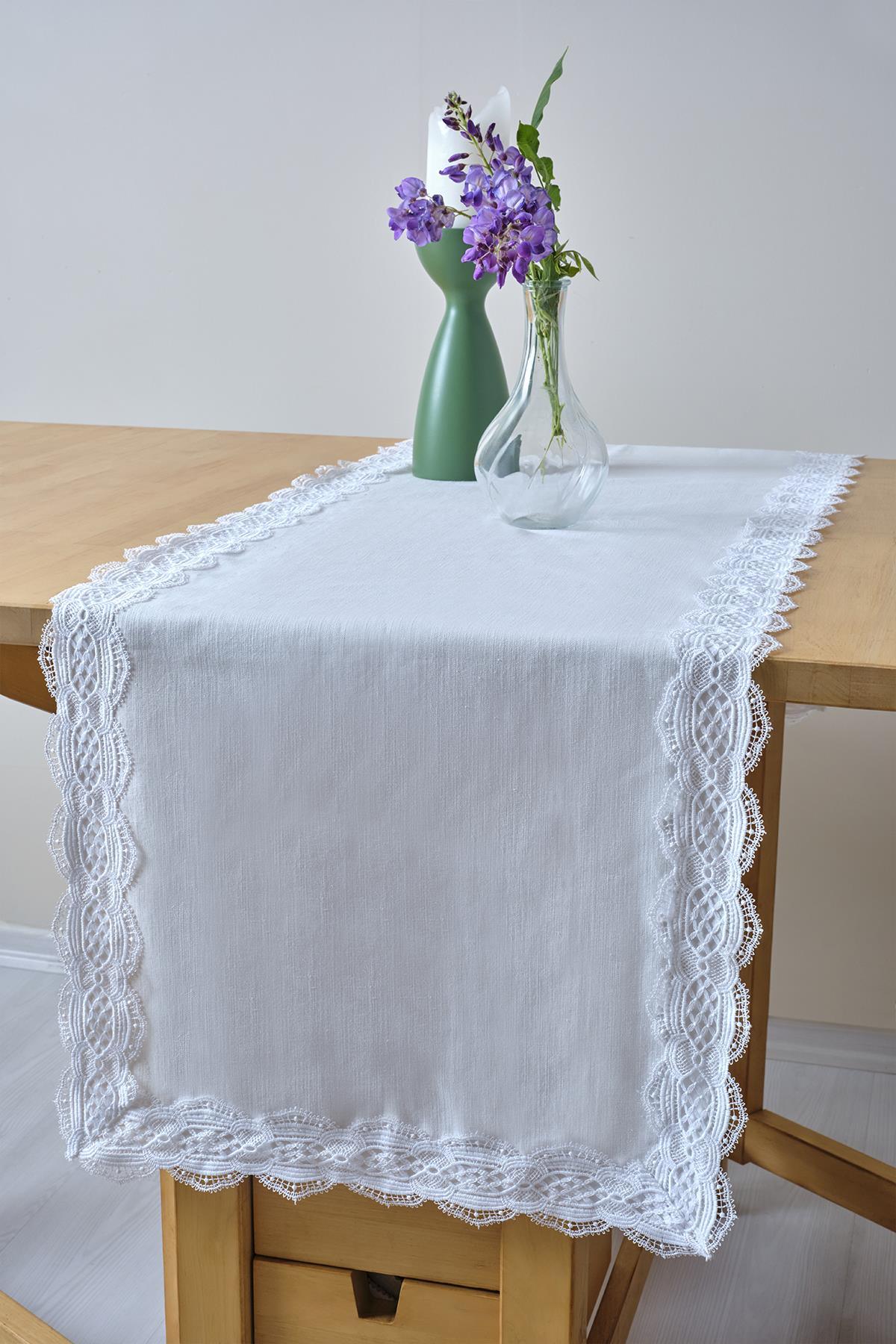 White table runner with lace trim, decorated with a glass vase and purple flowers on a wooden table