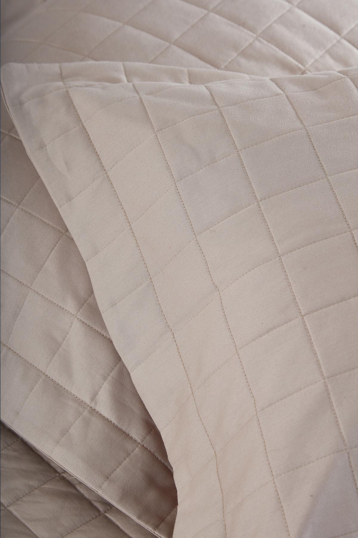 Close-up of a quilted beige double bedspread and pillowcase
