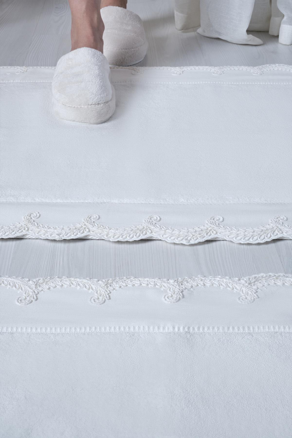 White, embroidered 2-piece bath mat set with lace edge detailing, on a modern floor