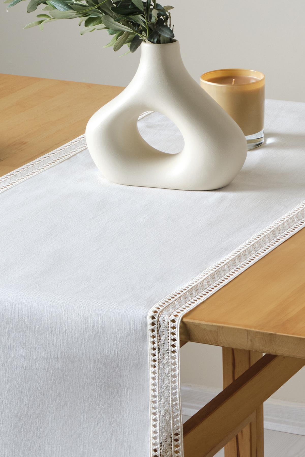 Decorative presentation with a white lace table runner, modern vase, and candle on a wooden table