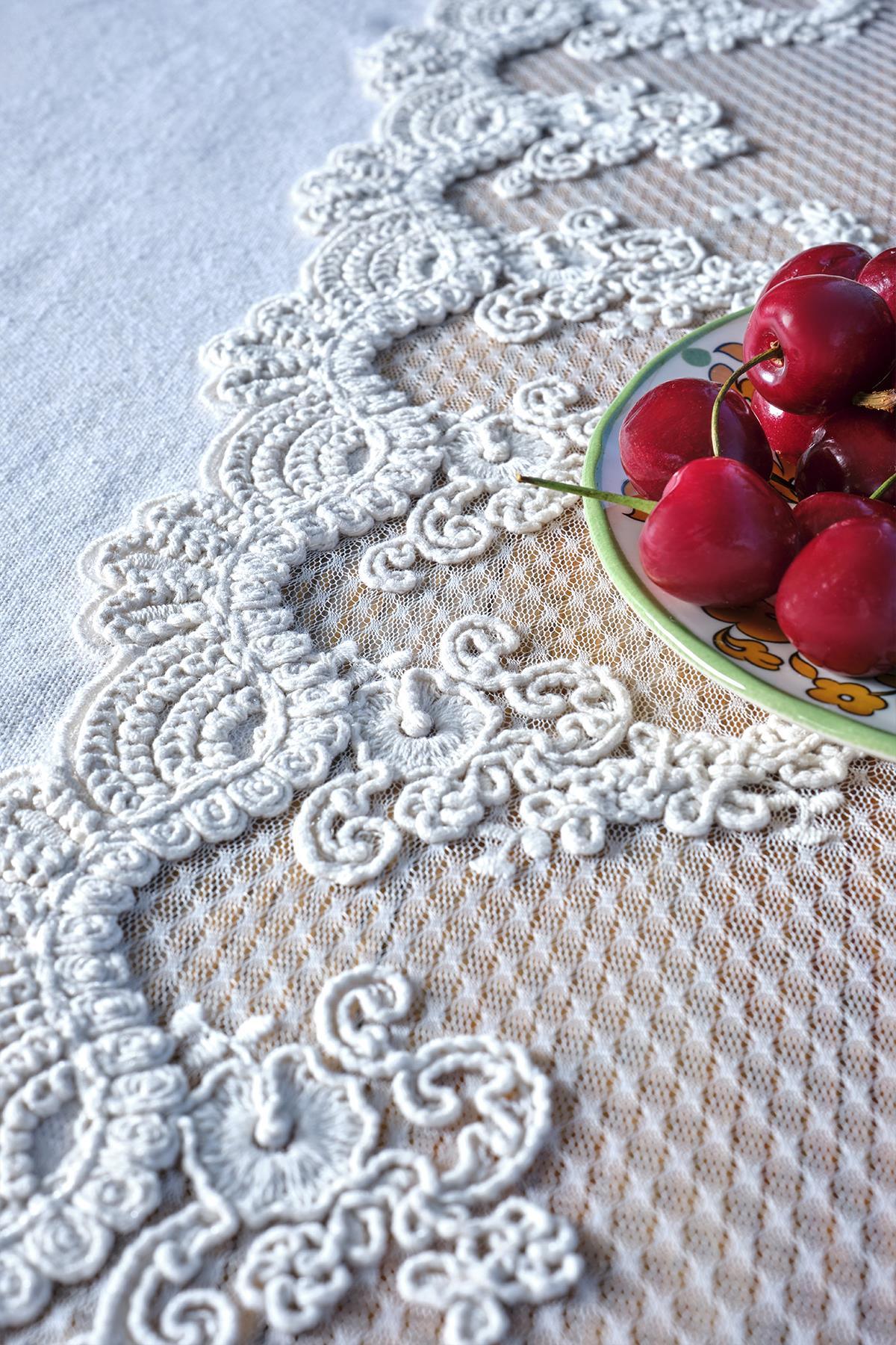 Close-up of a white lace-embroidered tablecloth with cherries on a plate.